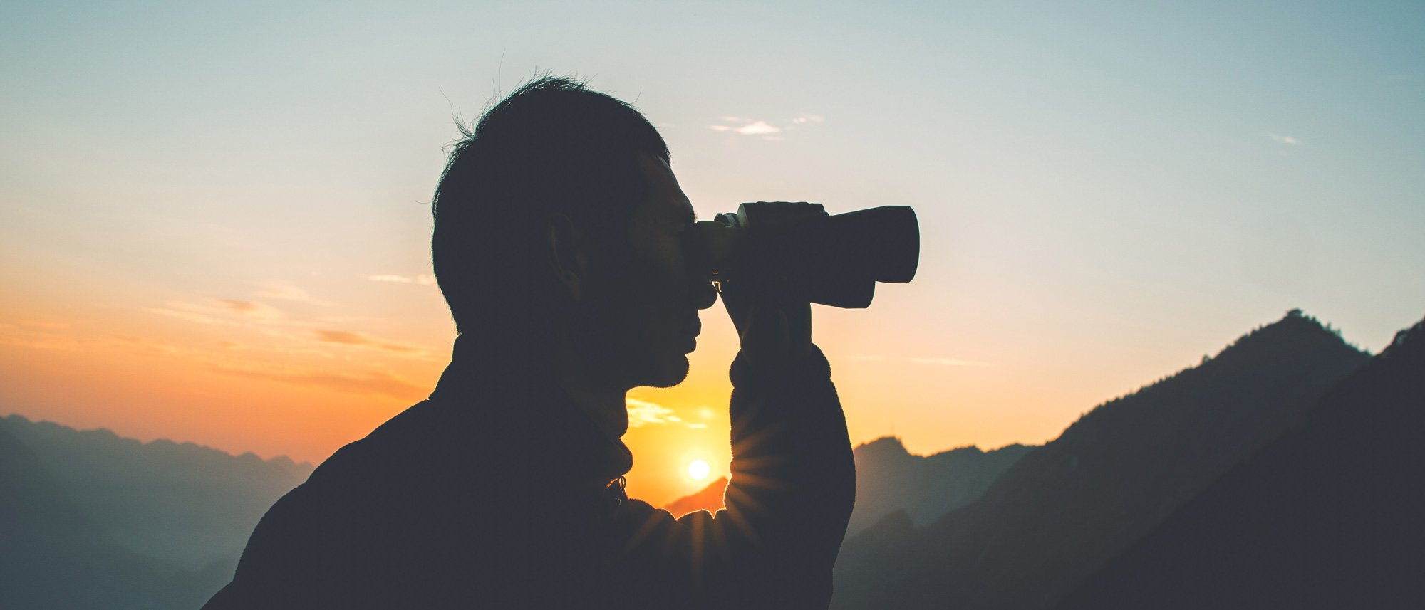 Man looking through binoculars at sunset