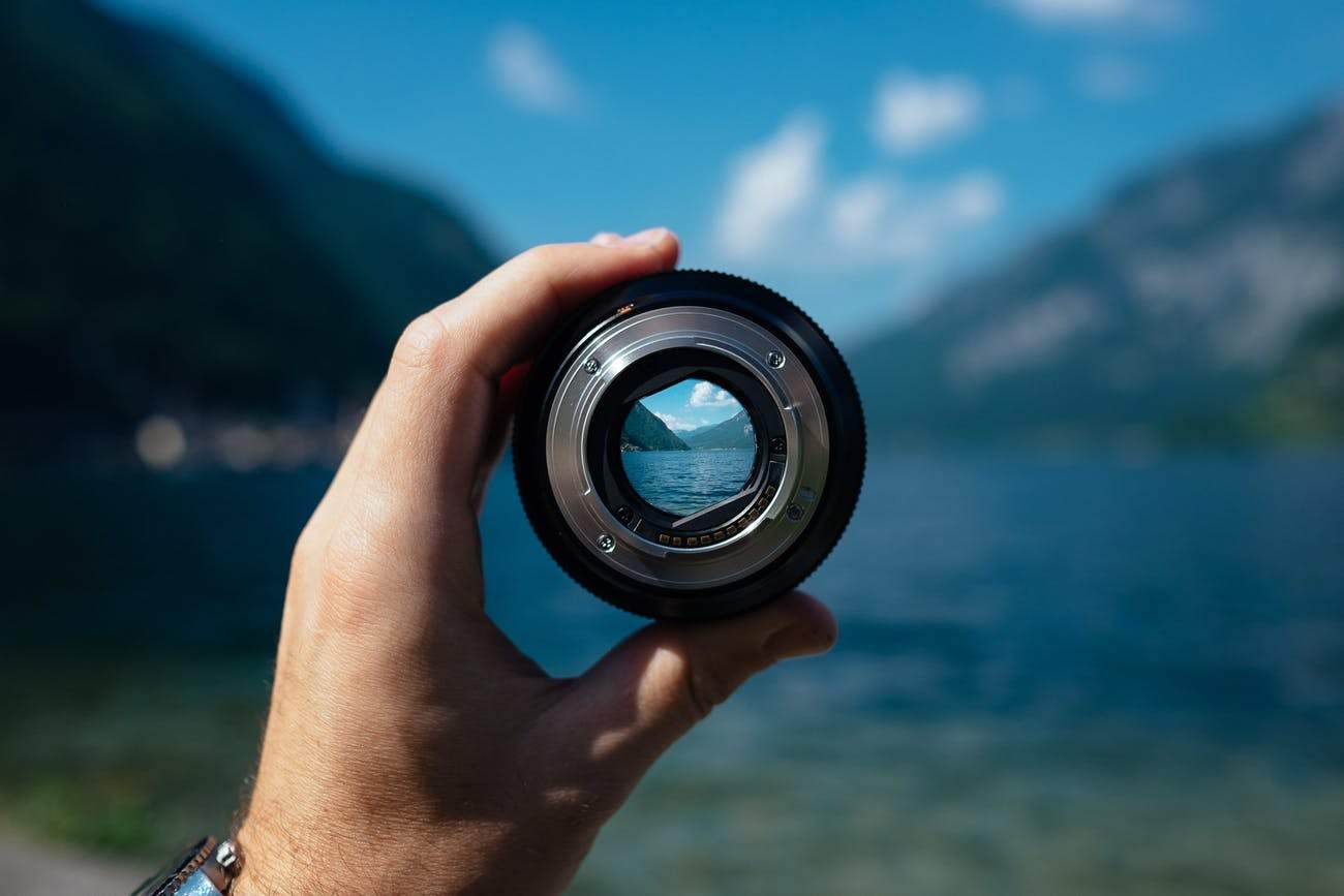 person holding lens in front of beach
