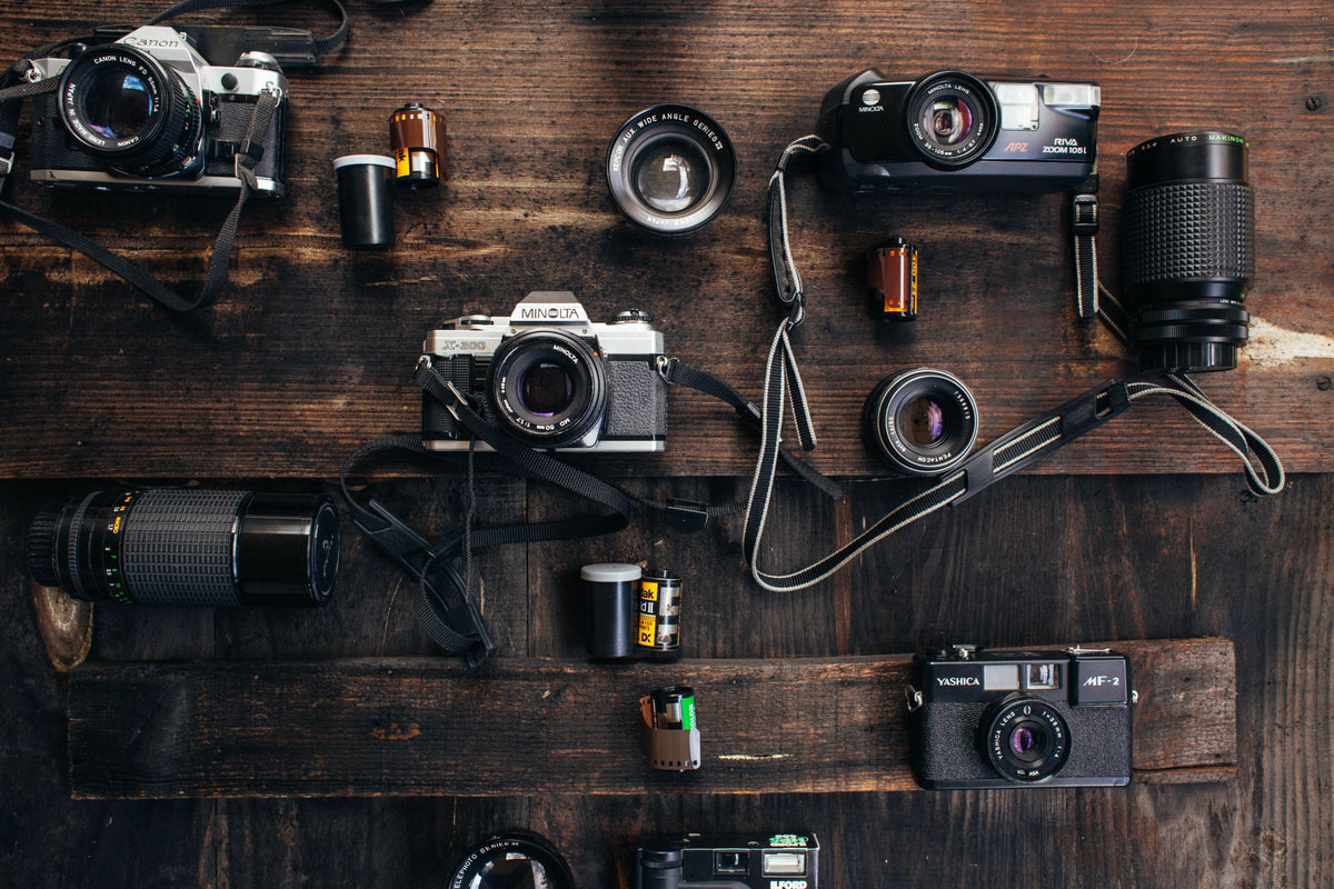 Film cameras, lenses and rolls of film laid out on a dark wooden table